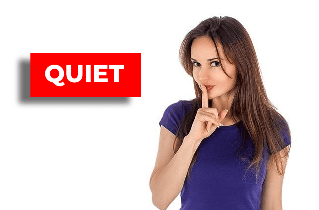 woman standing next to a sign that says "Quiet" with her index finger covering her lips
